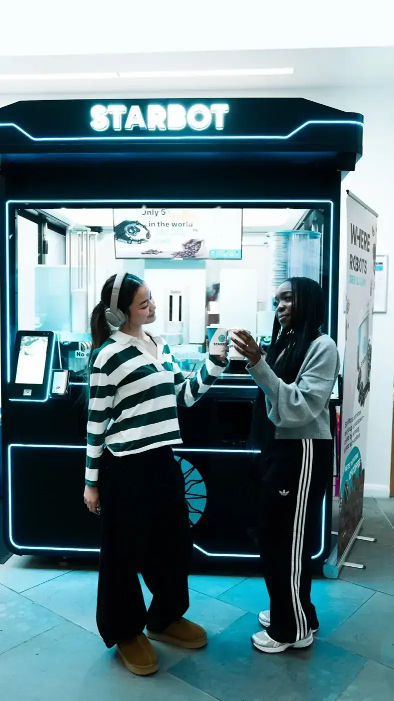 Two customers ordering at the lit Starbot kiosk on campus