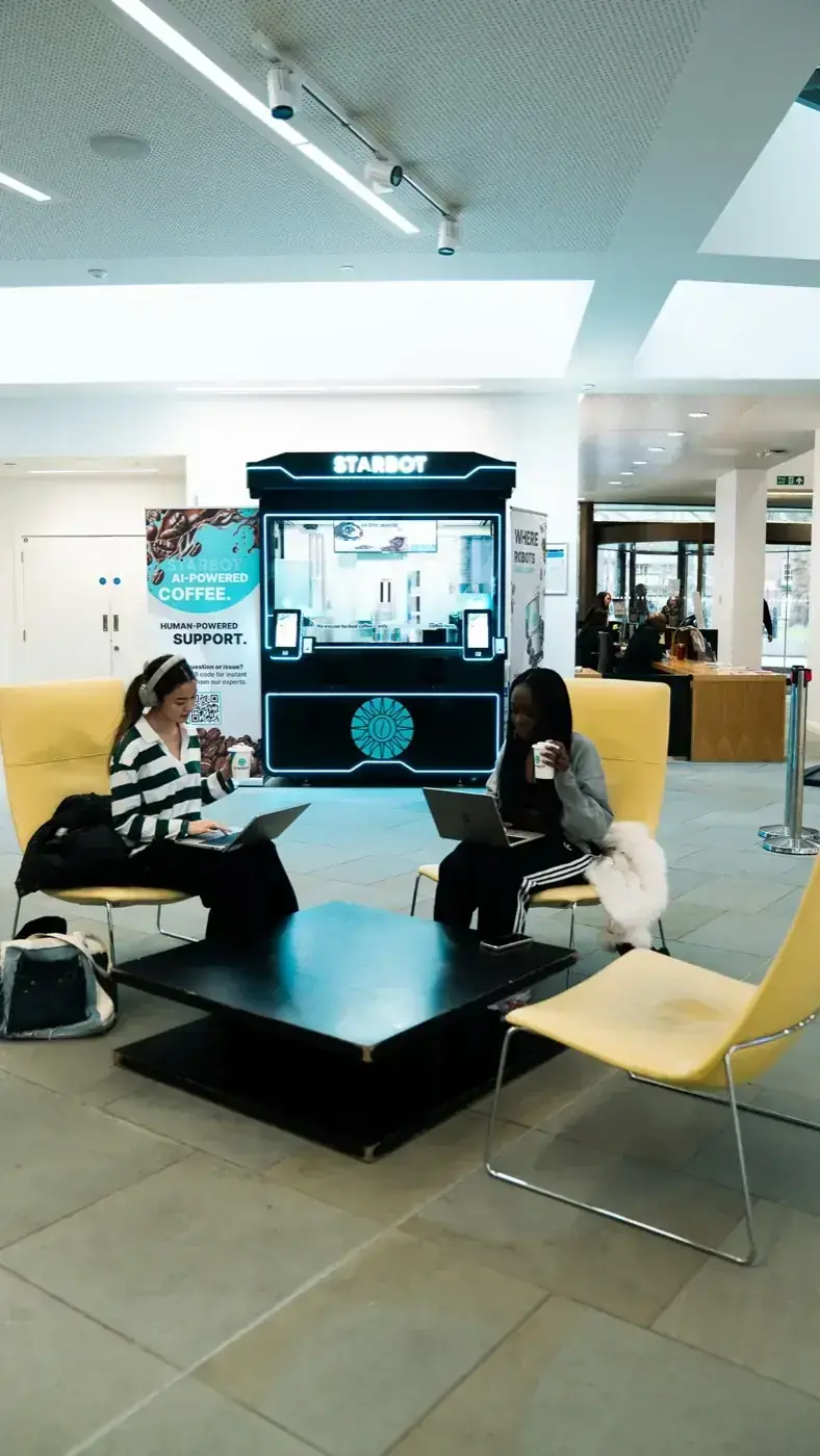 The Starbot kiosk standing in a university lobby beside study seating — the whole shop in one corner